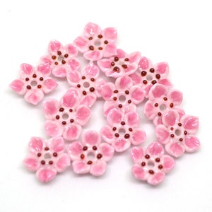 May include: Pink ceramic flower beads with a brown center. The beads are shaped like five-petal flowers.