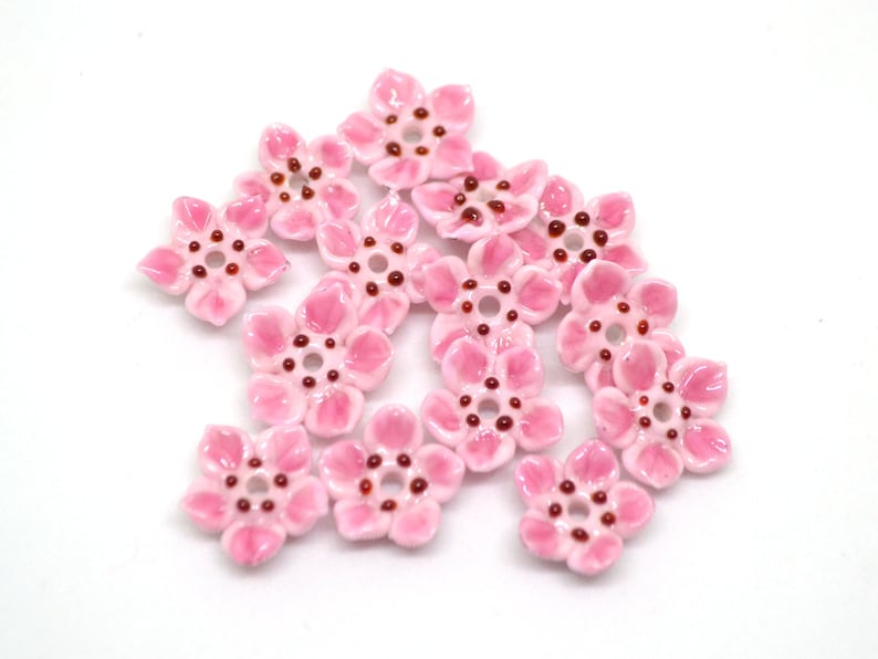 May include: Pink ceramic flower beads with a brown center. The beads are shaped like five-petal flowers.