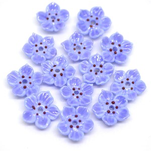 May include: A collection of 12 light blue flower-shaped glass beads with a brown center. The beads are arranged in a circle on a white background.