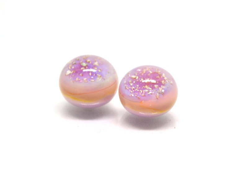 May include: Two small, round, iridescent glass beads with a pink and purple color scheme. The beads have a speckled appearance with gold flecks.