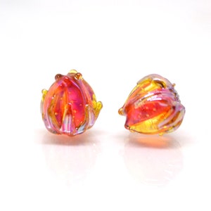 Puede incluir: Dos pequeñas cuentas de vidrio iridiscente en tonos de amarillo, naranja y rosa. Las cuentas tienen una forma texturizada y orgánica.