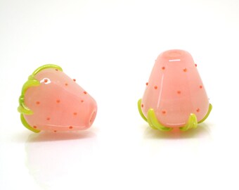 May include: Two pink glass strawberry shaped beads with green glass leaves. The beads are about 1 inch in diameter.