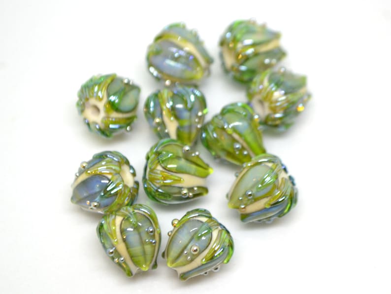 K&ouml;nnte beinhalten: Eine Sammlung von 10 gr&uuml;nen und wei&szlig;en Glasperlen mit perlmuttartigem Finish. Die Perlen sind in Form von kleinen Blumen mit einer strukturierten Oberfl&auml;che.