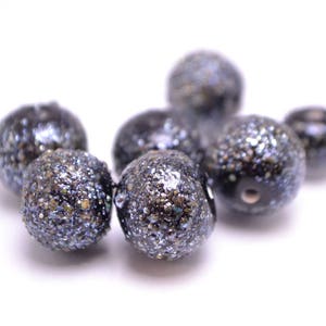 Op de afbeelding: Een groep zwarte en zilveren glitter kralen. De kralen zijn rond en hebben een getextureerd oppervlak.