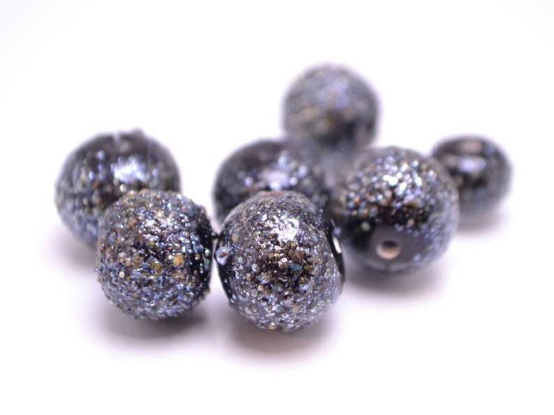 Op de afbeelding: Een groep zwarte en zilveren glitter kralen. De kralen zijn rond en hebben een getextureerd oppervlak.