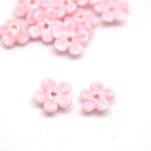 Peut inclure: Perles en forme de fleur rose avec un trou au centre. Les perles sont faites d'un matériau brillant et iridescent.