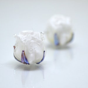May include: Two white glass rose-shaped beads with iridescent purple and blue accents.