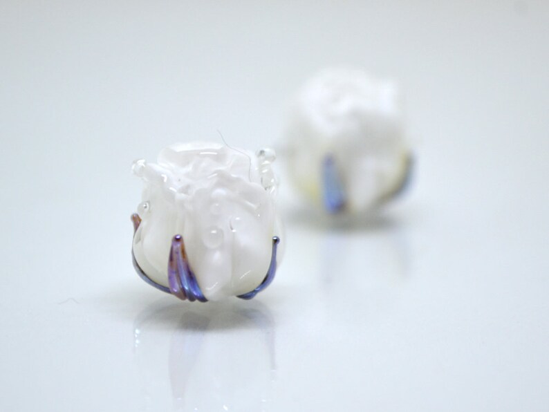 May include: Two white glass rose-shaped beads with iridescent purple and blue accents.