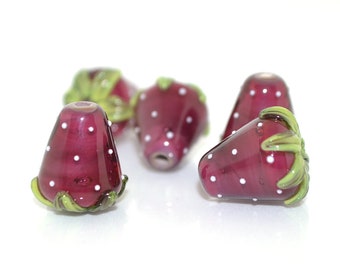 May include: Four glass strawberry-shaped beads with white polka dots and green leaves. The beads are a deep burgundy color.