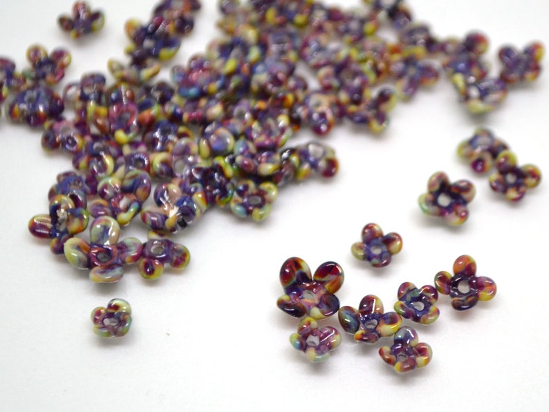 May include: A large quantity of small, colorful flower-shaped beads. The beads are made of glass and have a swirled, iridescent finish. The colors are predominantly purple, yellow, and red.