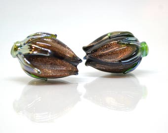 May include: Two iridescent glass beads in the shape of a flower bud. The beads are brown with green and blue accents.