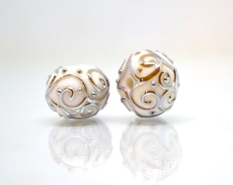 May include: Two white glass beads with a silver and gold swirl design.