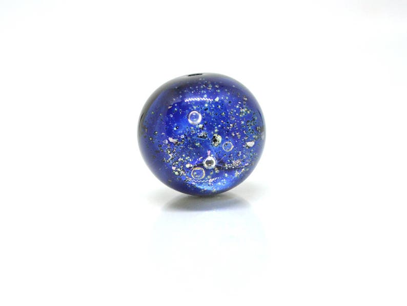 May include: A blue glass bead with silver flecks and air bubbles inside. The bead has a speckled, galaxy-like appearance.
