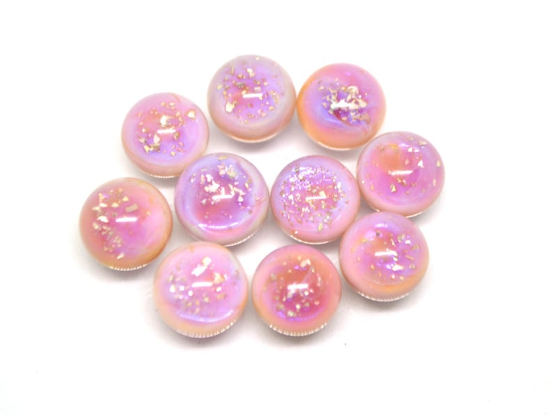 May include: Ten iridescent pink glass cabochons with gold flecks. The cabochons are round and have a smooth, glossy finish.