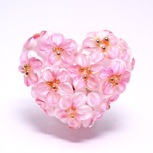 May include: A pink glass heart-shaped ornament with a cluster of pink flowers with gold centers.