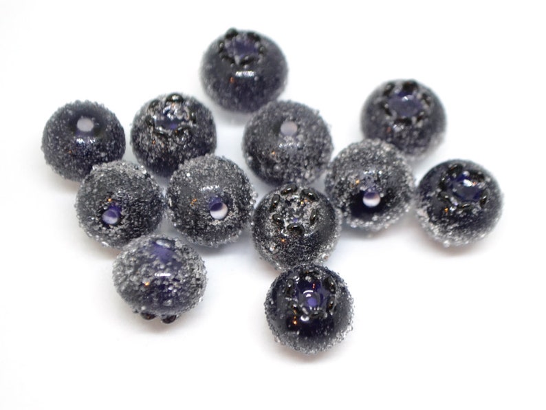 May include: A group of 11 dark blue glass beads, each with a slightly different shade of blue and a textured surface. The beads are arranged in a loose cluster on a white background.