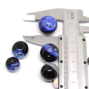 May include: Five blue and black glass beads with silver flecks. The beads are measured with a ruler in inches.
