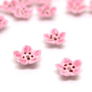 May include: Pink ceramic flower beads with brown centers. These beads are perfect for jewelry making or crafting.