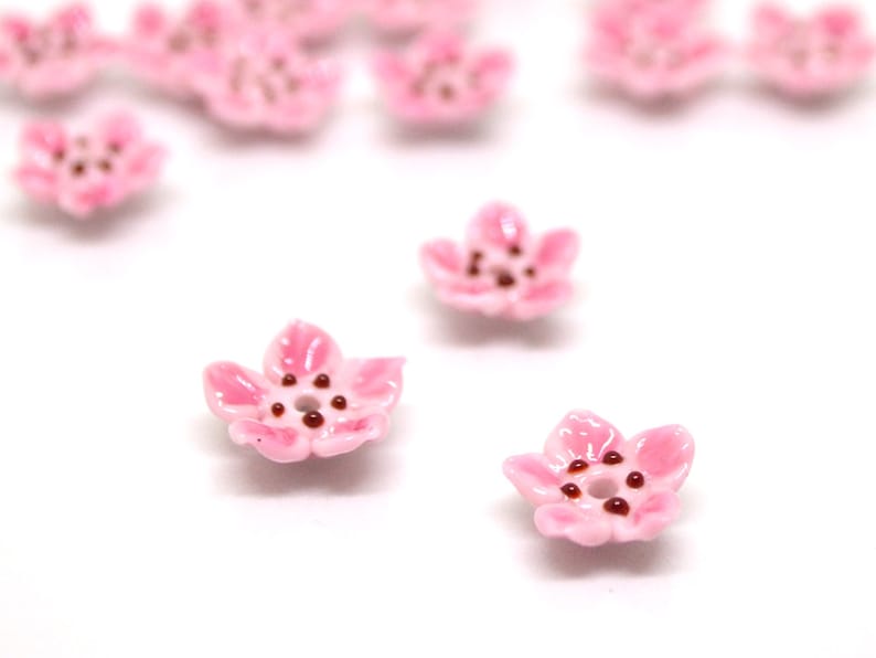 May include: Pink ceramic flower beads with brown centers. These beads are perfect for jewelry making or crafting.