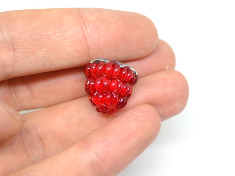 Puede incluir: Un charm de vidrio rojo en forma de frambuesa. El charm est&aacute; hecho de peque&ntilde;as cuentas redondas que se agrupan para formar la forma de una frambuesa.