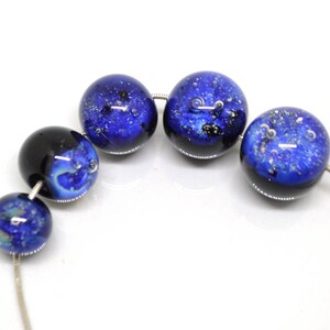 May include: A strand of blue glass beads with silver flecks and air bubbles. The beads are round and have a dark blue base with lighter blue swirls.