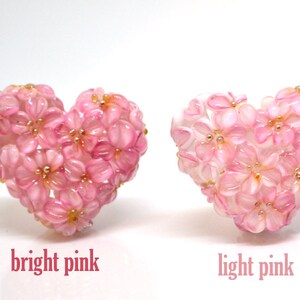May include: Two heart-shaped arrangements of pink flowers. The flowers on the left are a bright pink, while the flowers on the right are a light pink.