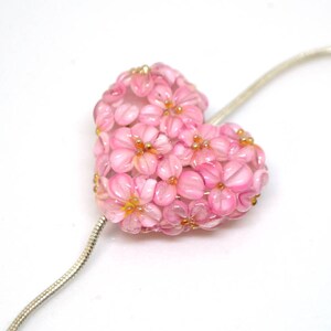 May include: A pink glass heart-shaped pendant necklace with a floral design. The pendant is made of many small pink glass flowers.