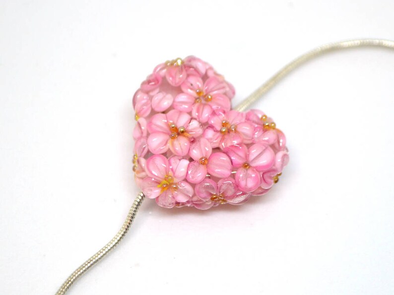 May include: A pink glass heart-shaped pendant necklace with a floral design. The pendant is made of many small pink glass flowers.
