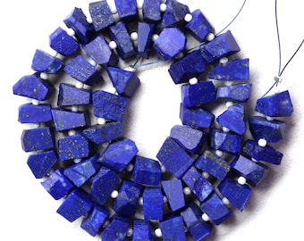 Könnte beinhalten: Eine Strang dunkelblauer Lapislazuli-Edelsteinkugeln mit weißen Abstandskugeln. Die Kugeln sind unregelmäßig geformt und haben eine raue, natürliche Textur.