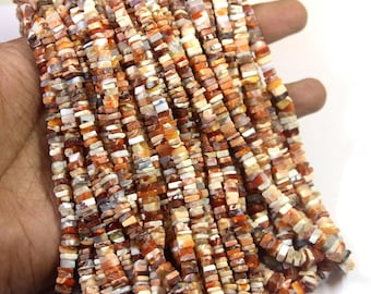 May include: Strands of small, square-cut beads in shades of orange, brown, and cream. The beads are strung together, creating a textured and colorful display. The beads are held in a hand.