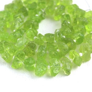 Puede incluir: Una hebra de cuentas de peridoto verde claro, cada cuenta est&aacute; facetada y tiene un aspecto &aacute;spero y natural.