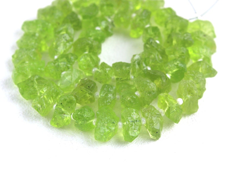 Puede incluir: Una hebra de cuentas de peridoto verde claro, cada cuenta est&aacute; facetada y tiene un aspecto &aacute;spero y natural.