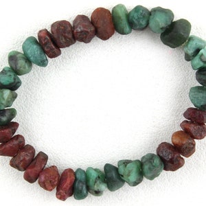 Pode incluir: Um bracelete feito de pequenas contas de pedras preciosas verdes e vermelhas irregulares. As contas são dispostas em um padrão de degradê, com as contas verdes no exterior e as contas vermelhas no interior.