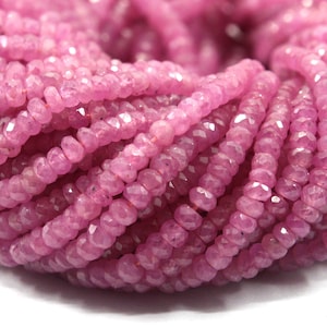 May include: A strand of pink faceted gemstone beads. The beads are small and round, and they are strung together on a clear thread. The beads are all the same size and shape, and they are arranged in a random order.