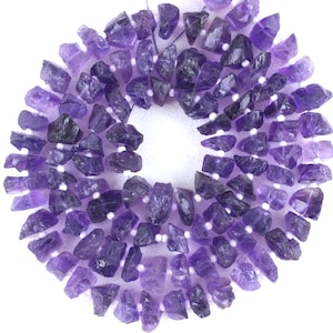 May include: A strand of purple amethyst gemstone beads, each bead is a rough, irregular shape. The beads are strung on a white thread.
