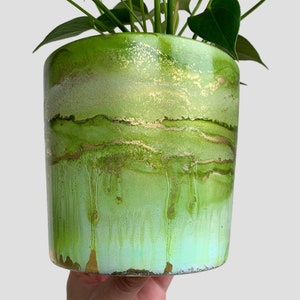May include: A green and gold planter with a unique marbled design. The planter is made of concrete and has a smooth, glossy finish.