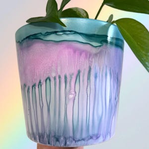 Könnte beinhalten: Ein hellblauer Keramiktopf mit einem marmornen Design in Rosa und Blau. Der Topf hat einen Tropfeffekt mit vertikalen Linien aus blauer und violetter Farbe.