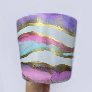 Puede incluir: Una maceta de cerámica blanca con un diseño ondulado abstracto en tonos de rosa, morado, azul y dorado.