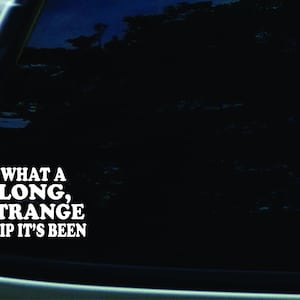 May include: A black car window with a white vinyl sticker that reads "What a long, strange trip it's been."