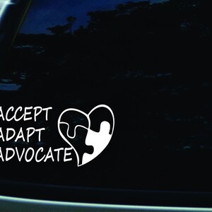 Pode incluir: Adesivo de vinil branco com as palavras "ACCEPT ADAPT ADVOCATE" e um design de peça de quebra-cabeça em forma de coração.