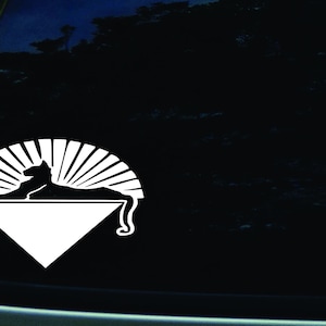 May include: White vinyl decal of a stylized cat lying down on a triangle with a sunburst behind it.