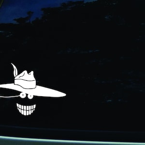 May include: A white vinyl decal of a smiling face wearing a wide-brimmed hat. The face has large eyes and a wide grin.
