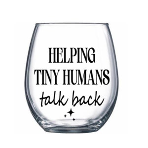 May include: A clear glass wine glass with the text "Helping Tiny Humans Talk Back" printed on it.