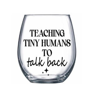 May include: A clear glass wine glass with the text "TEACHING TINY HUMANS TO talk back" printed on it.