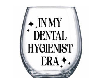 May include: A clear glass wine glass with the text "In My Dental Hygienist Era" printed on it. The text is in black and there are two small stars on either side of the text.