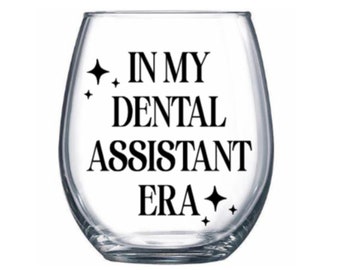 May include: A clear glass wine glass with the text "In My Dental Assistant Era" printed in black. The text is surrounded by small black stars.