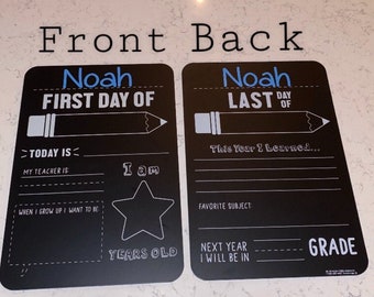 May include: Two black chalkboard signs with white writing. The first sign says "Noah First Day Of" and has a pencil icon. The second sign says "Noah Last Day Of" and has a pencil icon. Both signs have space for writing.