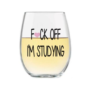May include: A clear glass wine glass with the text "F♡CK OFF I'M STUDYING" printed on it.
