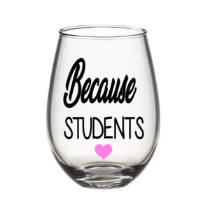 May include: A clear glass wine glass with a black vinyl decal that reads "Because Students" with a pink heart below the text.