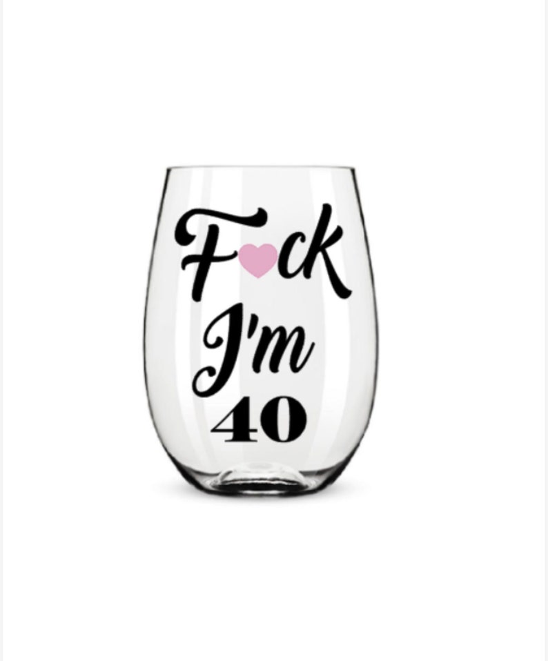 May include: A clear stemless wine glass with black text that reads "F*ck I'm 40" with a pink heart replacing the letter "o". The glass is empty and sits against a white background.
